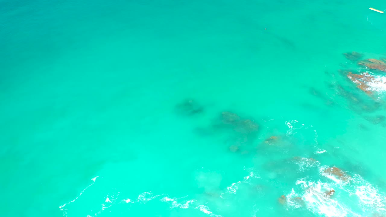Top-down Dreams Los Cabos ocean view with white foam curling around submerged rocks near the lower right and no visible people.