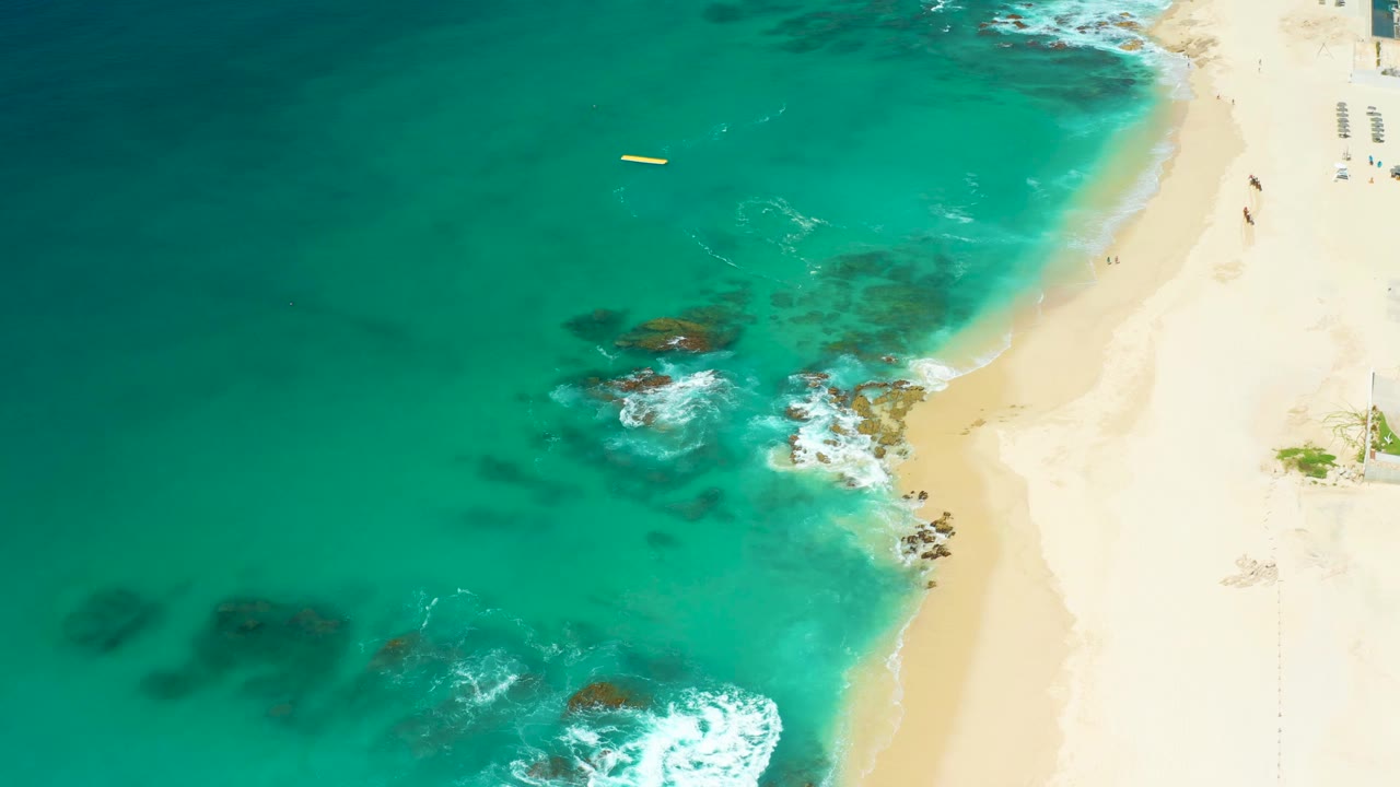 Drone view of green-blue surf washing around rocks on a sandy shore