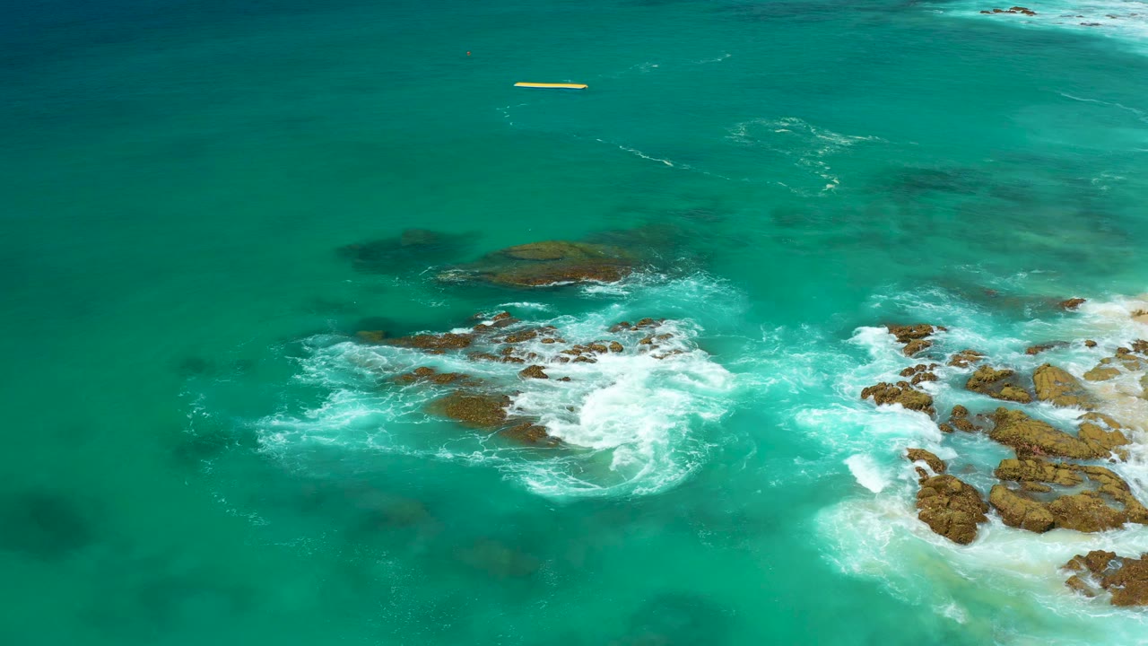 Overhead view of turquoise water and white surf breaking around brown coastal rocks at Dreams Los Cabos, with no visible people.