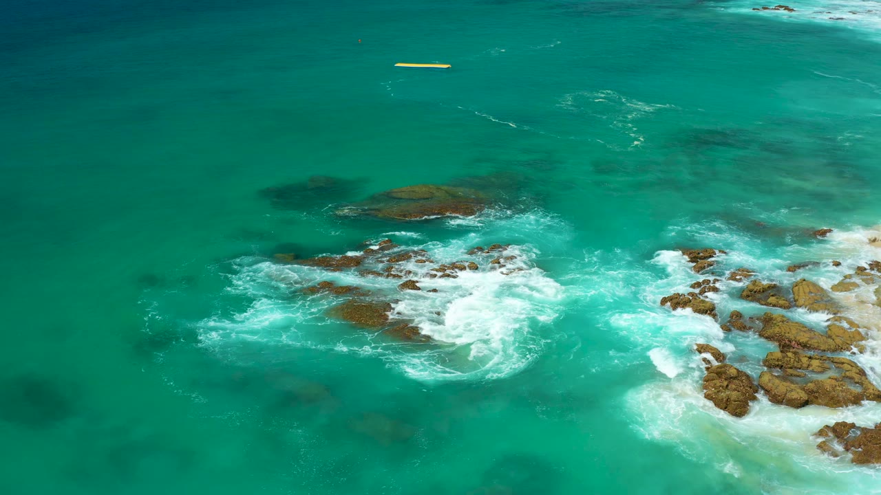 White foam spreads across submerged and exposed rocks in turquoise water at Dreams Los Cabos, with open sea across the top and no visible people.