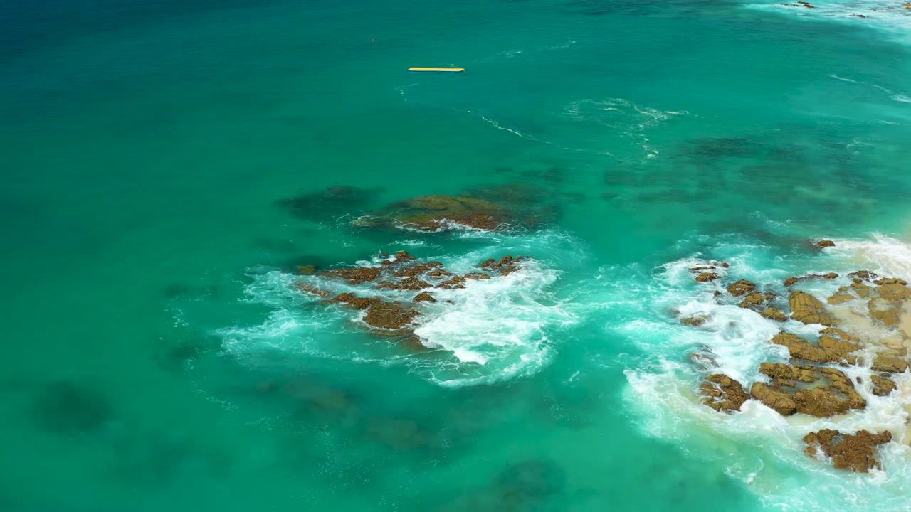 Wave foam circling rocks beside turquoise water