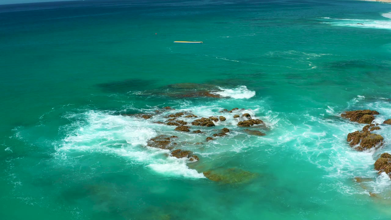 At Dreams Los Cabos in Baja California Sur, turquoise water breaks into white foam around low rocky outcrops, with no visible people.