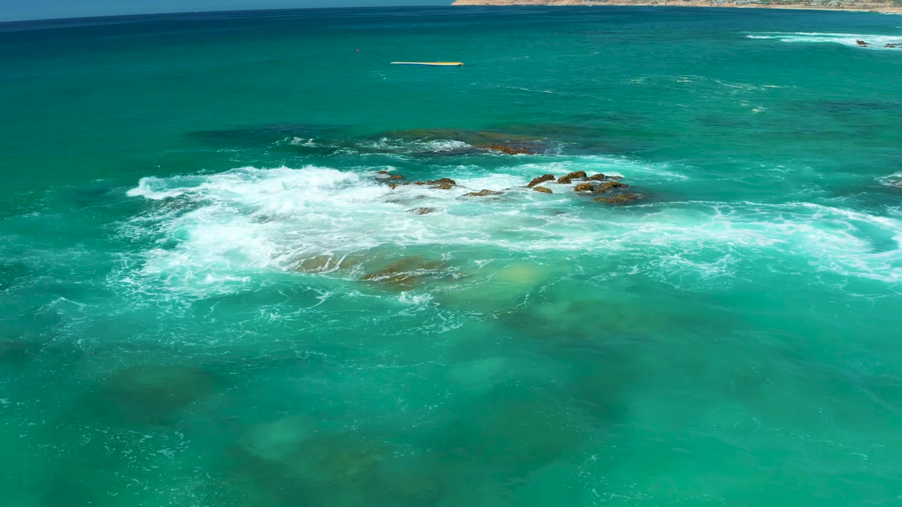 Aerial view of foamy waves sweeping across shallow rocks.