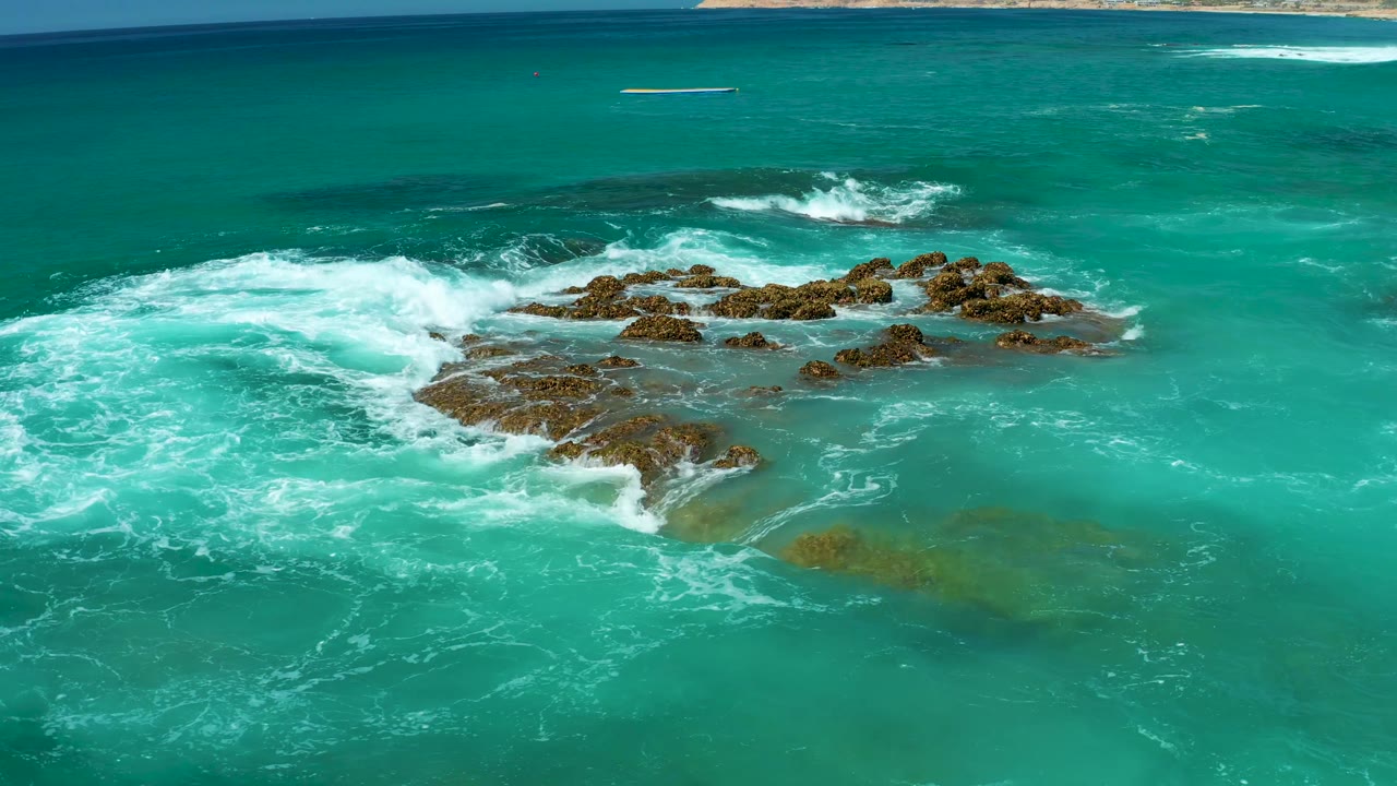 Surf spreading around low rocks in clear ocean.