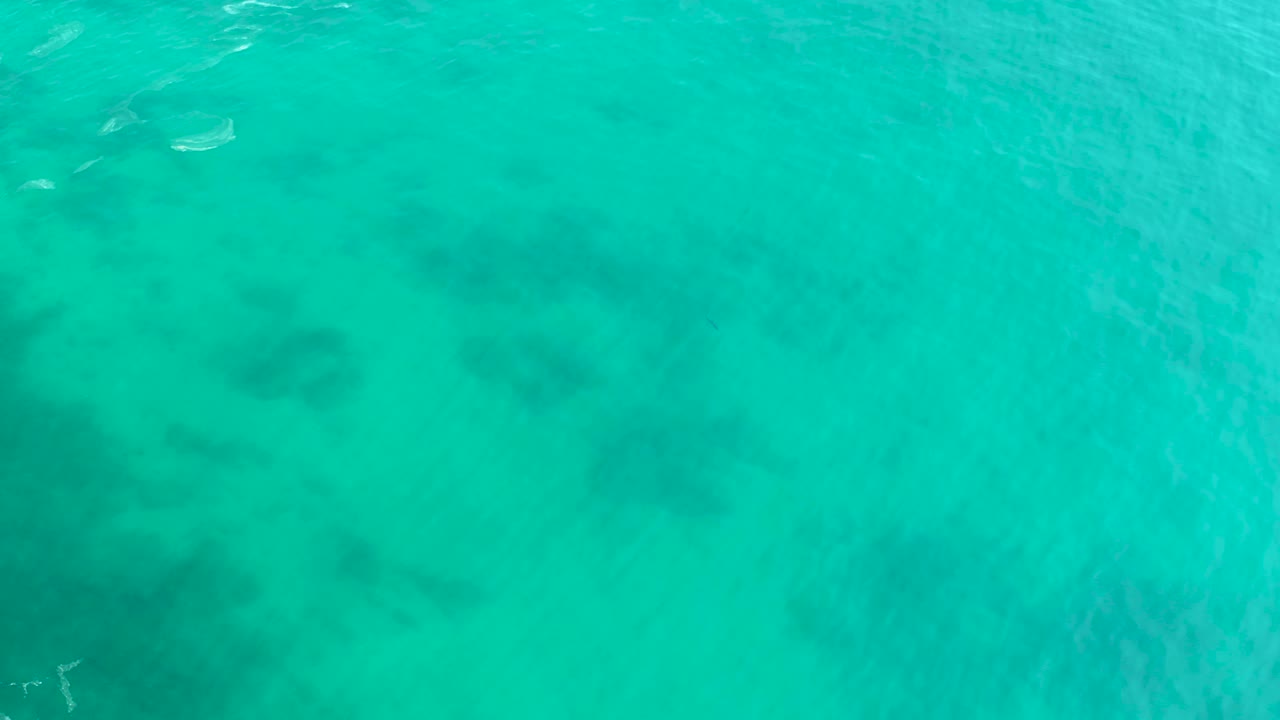 Clear teal water over reef shapes at Shipwrecks Los Cabos, with a small partial white boat near the upper edge and no visible people.