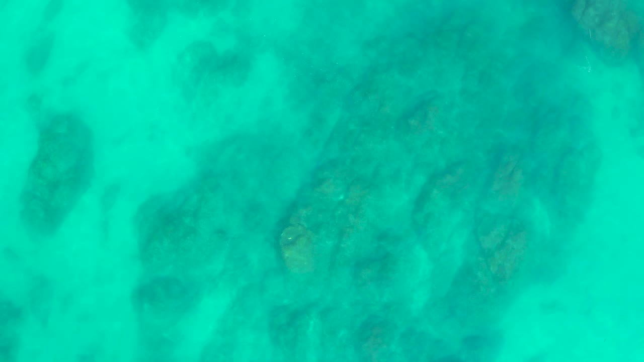 Clear blue-green ocean water reveals soft-edged underwater rock shapes at Shipwrecks Los Cabos, with no visible people or boats.