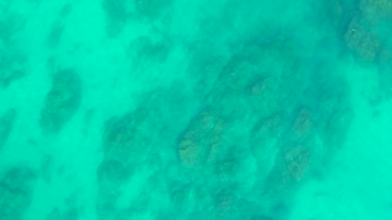 Shallow turquoise water covers blurred seabed rocks in a top-down Shipwrecks Los Cabos view, with no visible people in the frame.