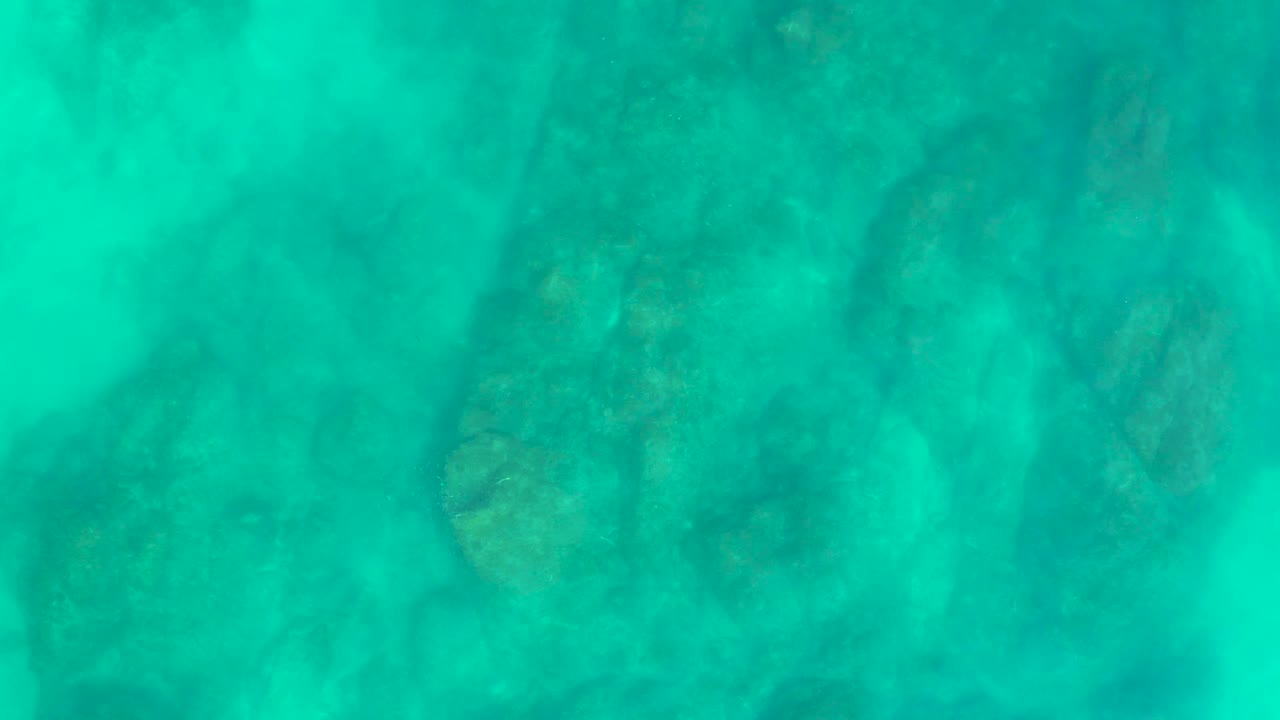 Clear green-blue water sits over rounded seabed rocks and soft sand patches at Shipwrecks Los Cabos, with no visible people.