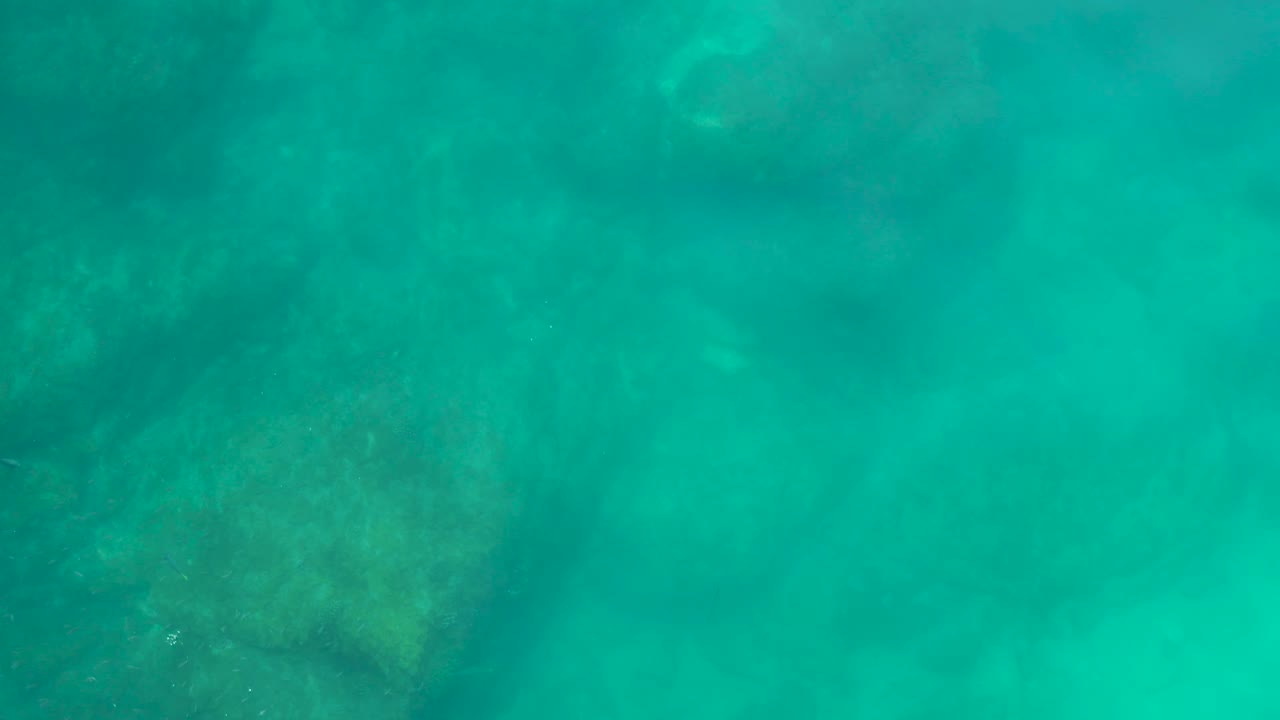 Turquoise underwater view at Shipwrecks Los Cabos with dim rocky seabed shapes beneath the water and no visible people.