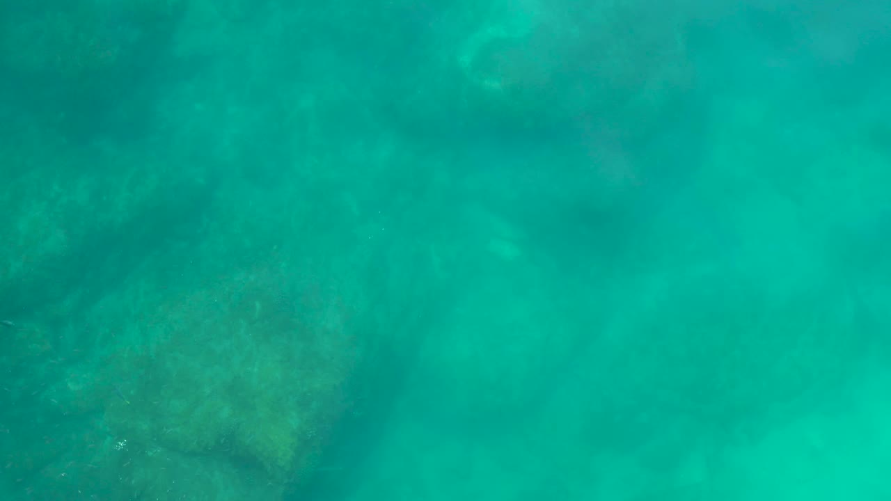 Clear green-blue water at Shipwrecks Los Cabos reveals darker rock forms on the seabed, with no visible people.
