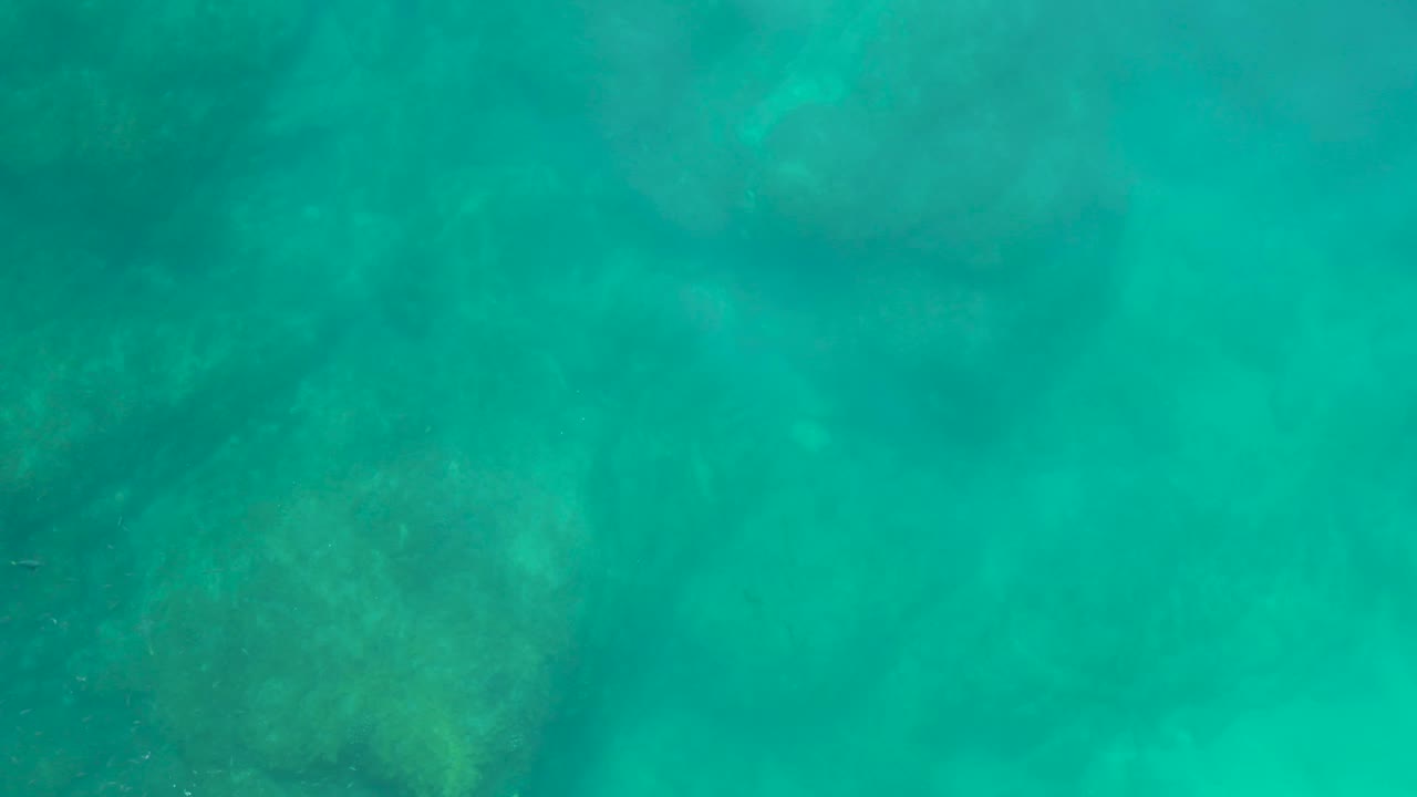 Underwater frame from Shipwrecks Los Cabos showing muted rock and coral-like textures under turquoise water, with no visible people.
