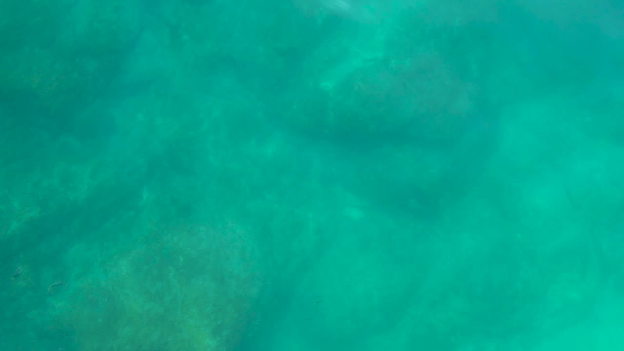 Bright turquoise underwater view at Shipwrecks Los Cabos with a broad rocky patch visible near the lower frame and no visible people.