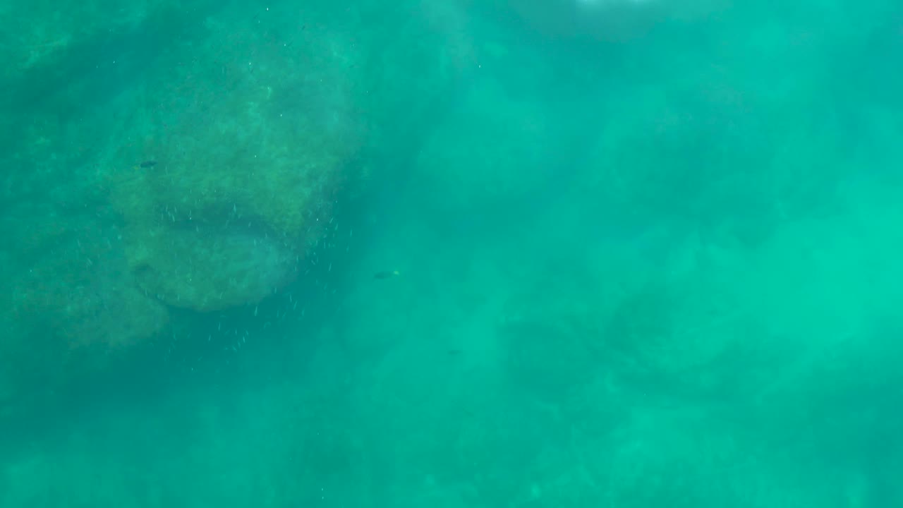 Rock formation under green-blue water with soft haze around it.