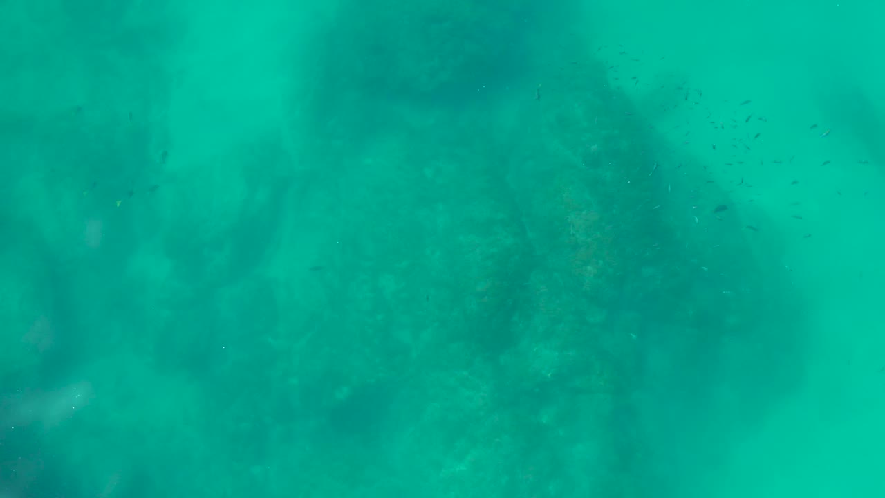 Turquoise underwater view over a rocky seabed at Shipwrecks Los Cabos, Baja California Sur, Mexico, with suspended particles and no visible people.