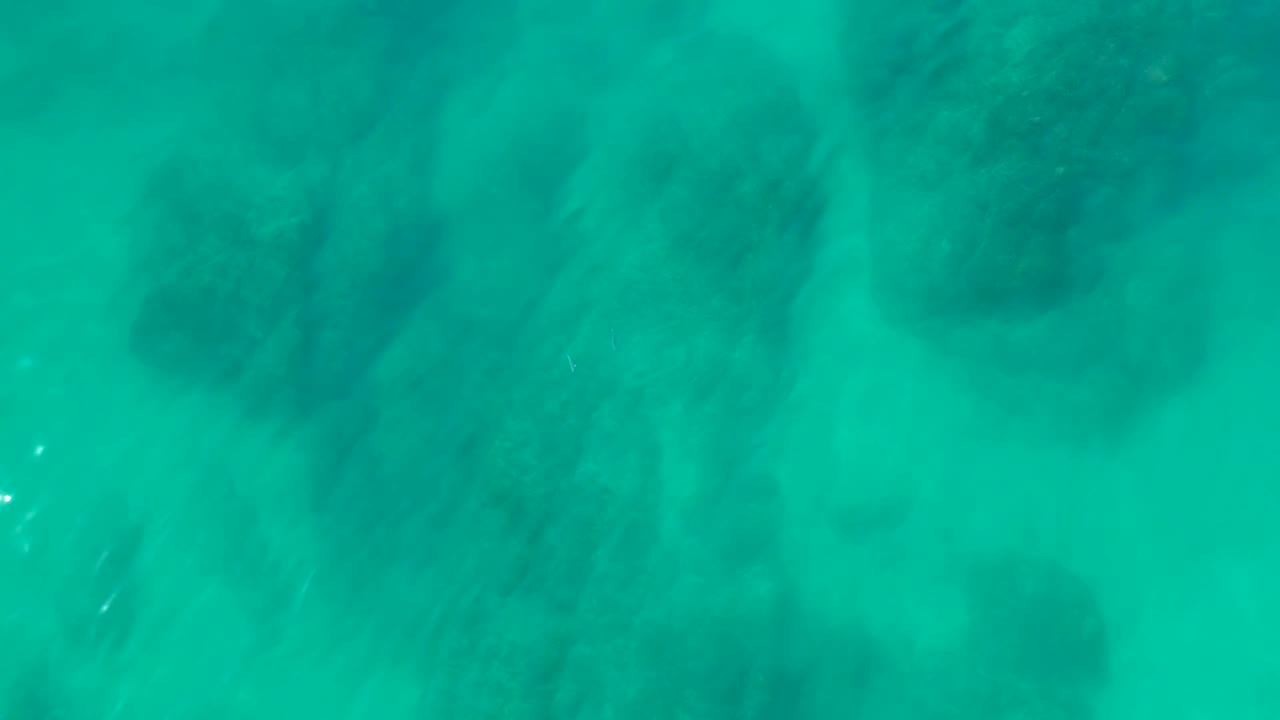 Turquoise ocean water at Shipwrecks Los Cabos reveals shadowy underwater rocks beneath a lightly rippled surface, with no visible people.