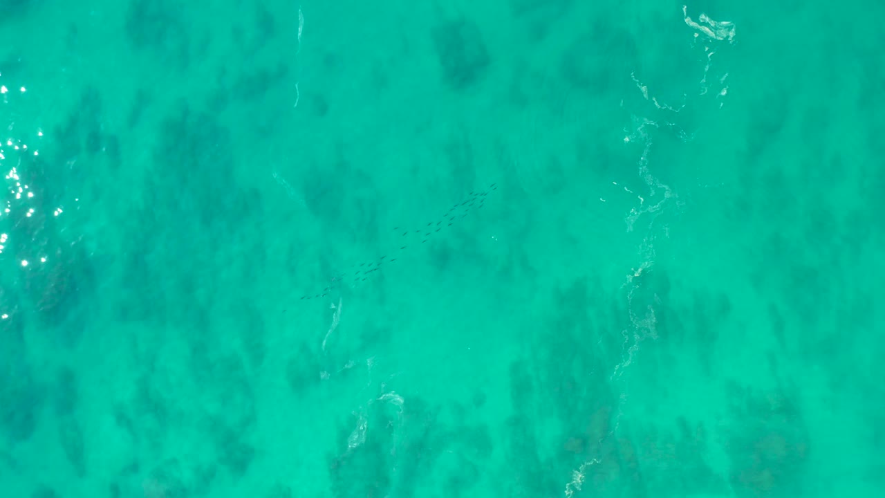 Turquoise water with dark underwater patches and small foam streaks.