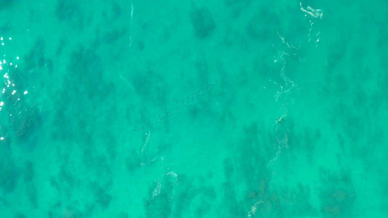 Clear aqua water fills the frame at Shipwrecks Los Cabos, with darker seabed marks beneath the surface, bright sunlight glints near the upper area, and no visible people.