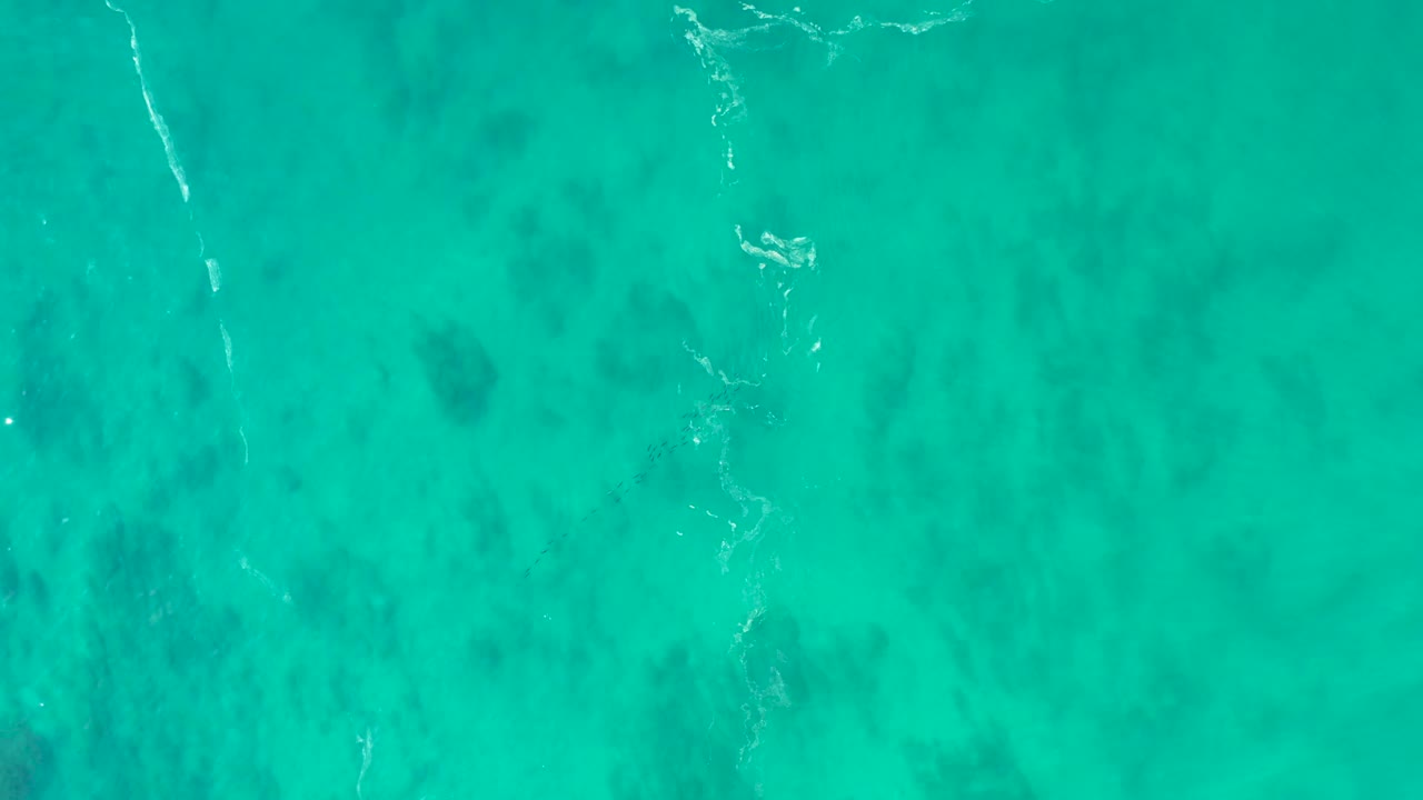 Clear teal ocean water at Shipwrecks Los Cabos, Mexico, shows a faint white ripple line over darker underwater patches with no visible people.