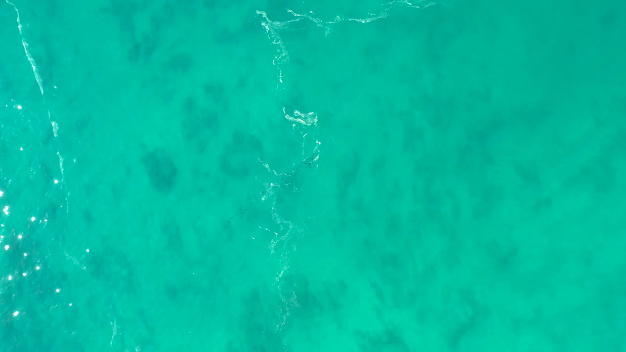 Clear blue-green water at Shipwrecks Los Cabos fills the frame, with small bright sun glints beside a narrow white water line and no visible people.