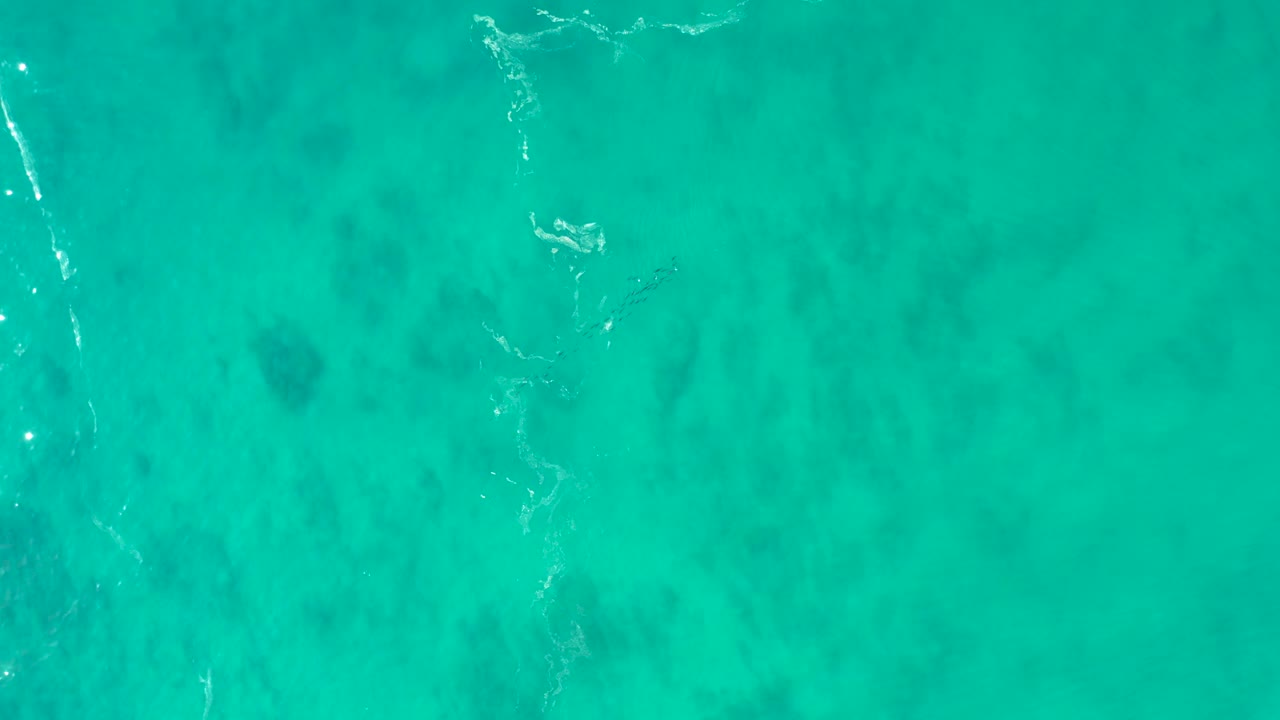 Top-down turquoise ocean water with faint seabed patches and thin foam