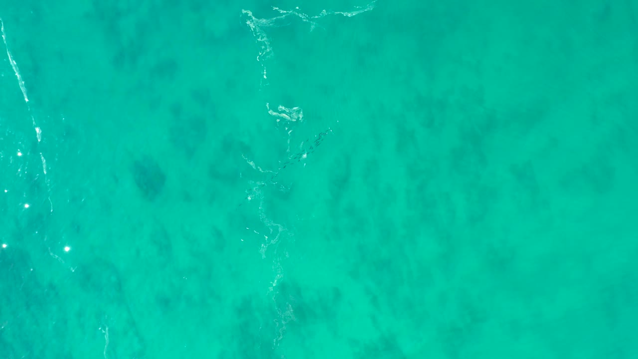 Shipwrecks Los Cabos shallow turquoise water appears from above with white foam streaks near the left side and darker submerged patches, no visible people.