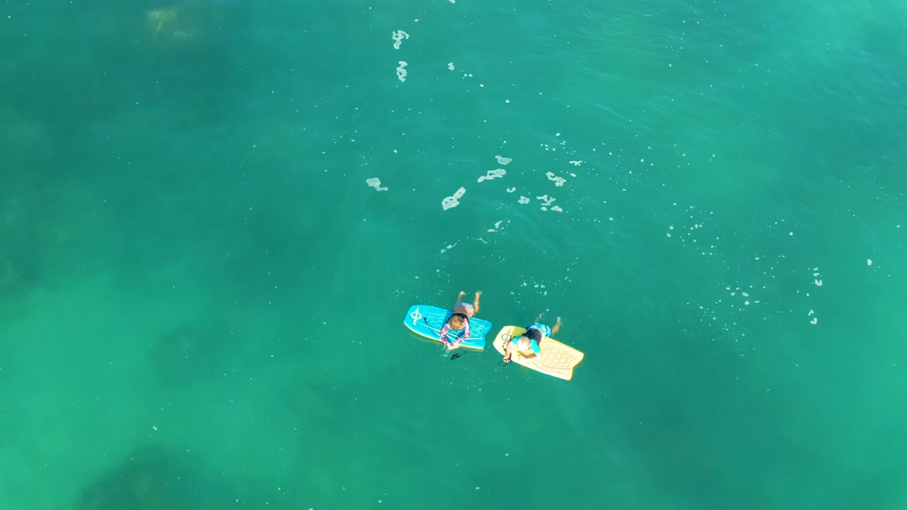 Two board riders floating over clear green-blue water.