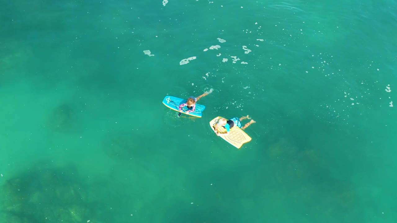 Aerial view at Shipwrecks Los Cabos showing the blue and pale yellow boards slightly separated in turquoise water, with darker underwater shapes visible below the surface.