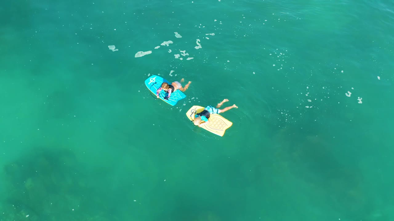 Two floating boards with people over clear green-blue water.