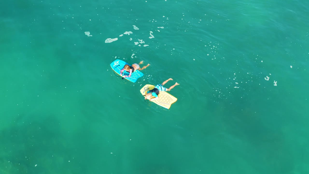 Overhead frame of the two board riders at Shipwrecks Los Cabos, with the blue board slightly above the beige board in calm turquoise water.