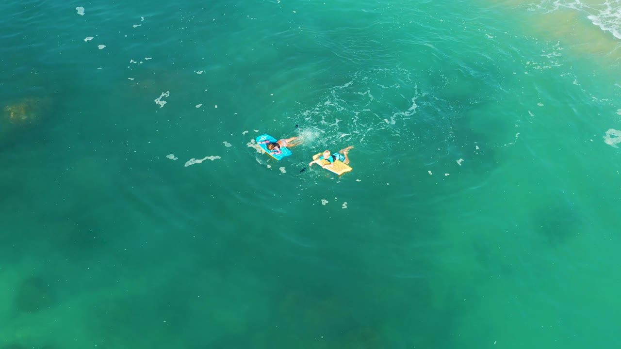 At 0:02, the people remain separated slightly in the upper portion of the overhead Shipwrecks Los Cabos frame, with the blue bodyboard left of the light yellow float.