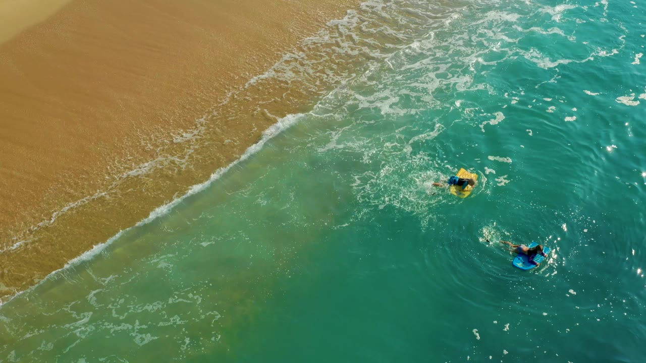 Bodyboarders floating offshore as foam reaches the sand