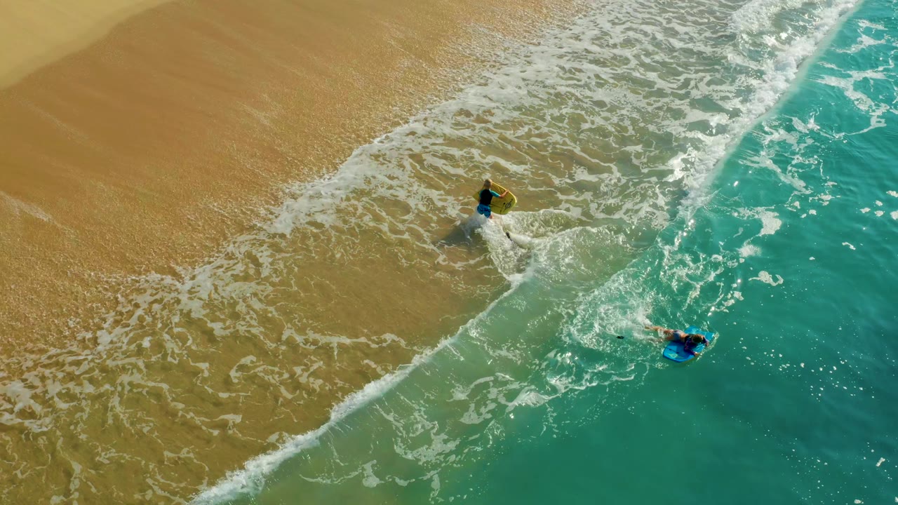 Two bodyboarders remain near the diagonal surf line.