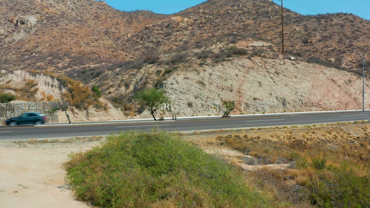 Dark car moving along road below rocky hills