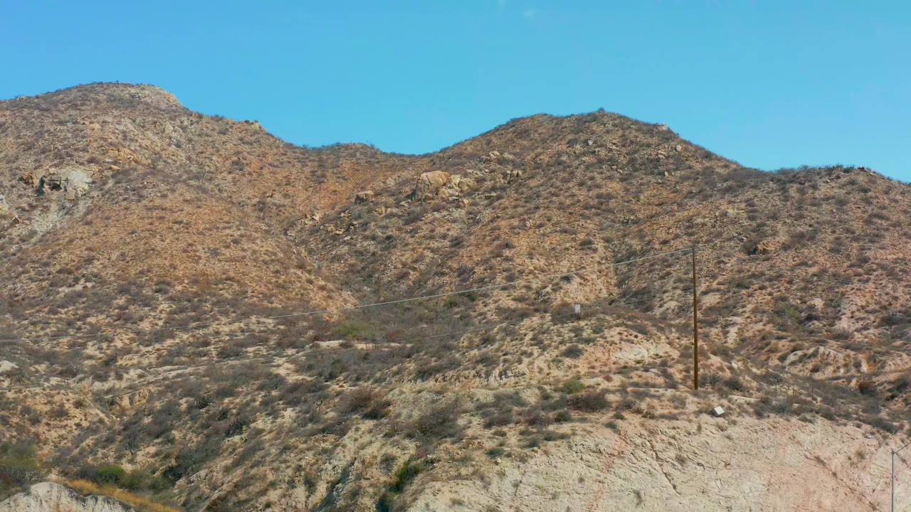 At Marquis Los Cabos, Mexico, the same rocky hillside remains in view while a small white spot appears high in the blue sky, with no visible people.