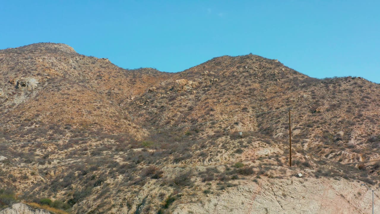 At Marquis Los Cabos, Mexico, tan and brown ridges with scattered scrub stretch across the frame below clear blue sky, with no visible people.