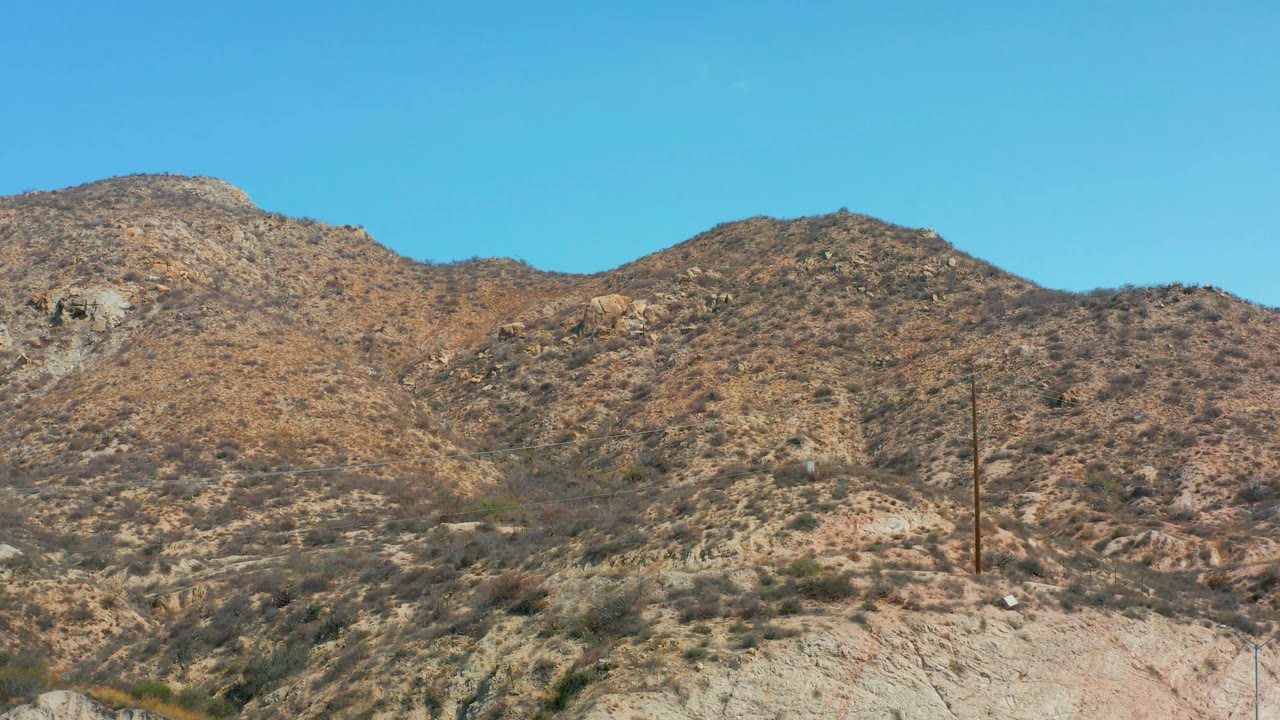 At Marquis Los Cabos, Mexico, pale foreground ground rises into rocky scrub hills, with a utility pole on the slope and no visible people.
