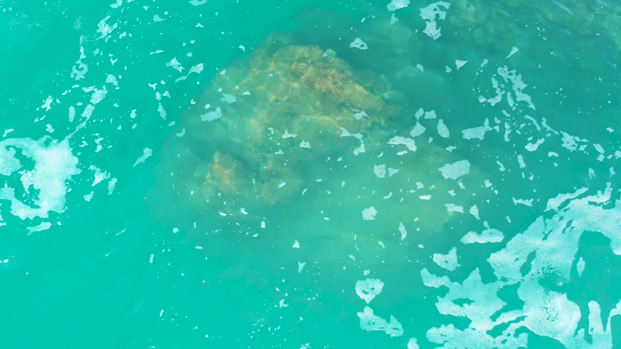 Turquoise water and white foam over a submerged rock