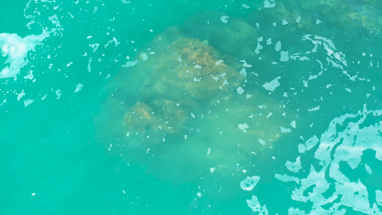 Turquoise water over a submerged rock with white surface foam.