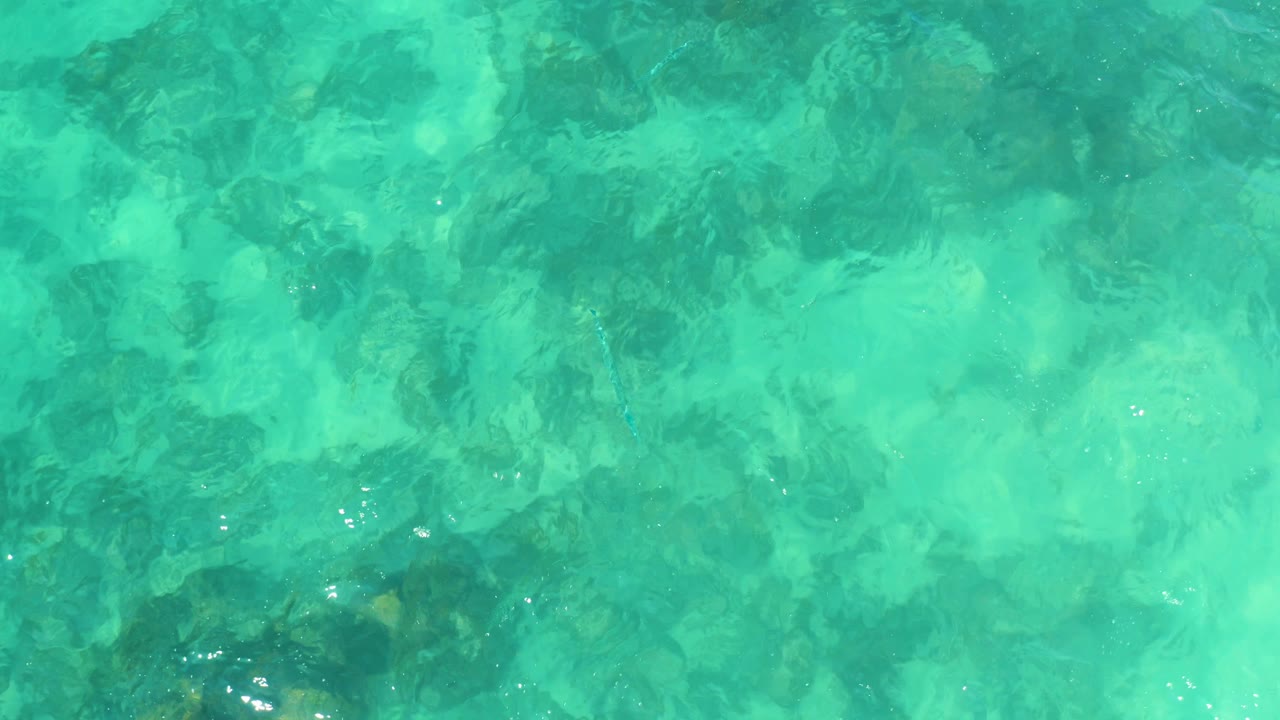 Turquoise shallow water over dark rocky seabed patches.