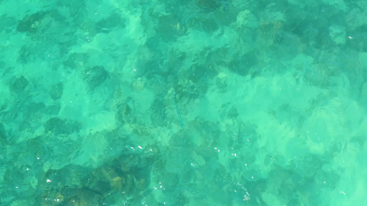 Pale turquoise shallows at Marquis Los Cabos reveal a rocky seabed through moving surface texture and scattered highlights, with no visible people.