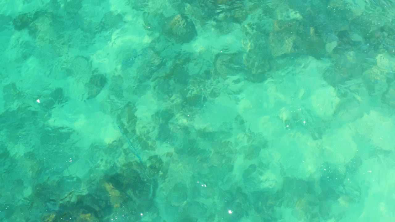 Clear shallow water at Marquis Los Cabos, Mexico, with pale aqua areas, darker submerged rocks, small bright glints, and no visible people.