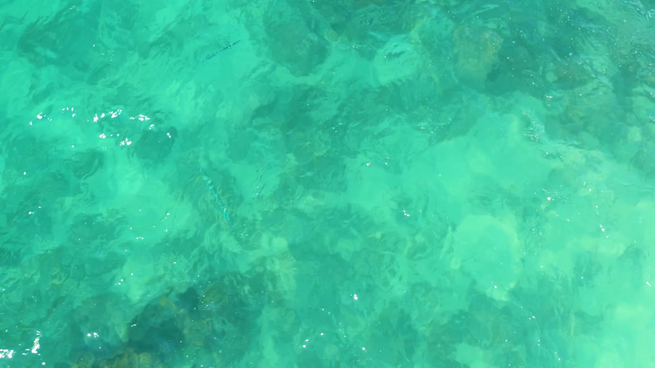 Aqua water surface with rocks visible through moving ripples.