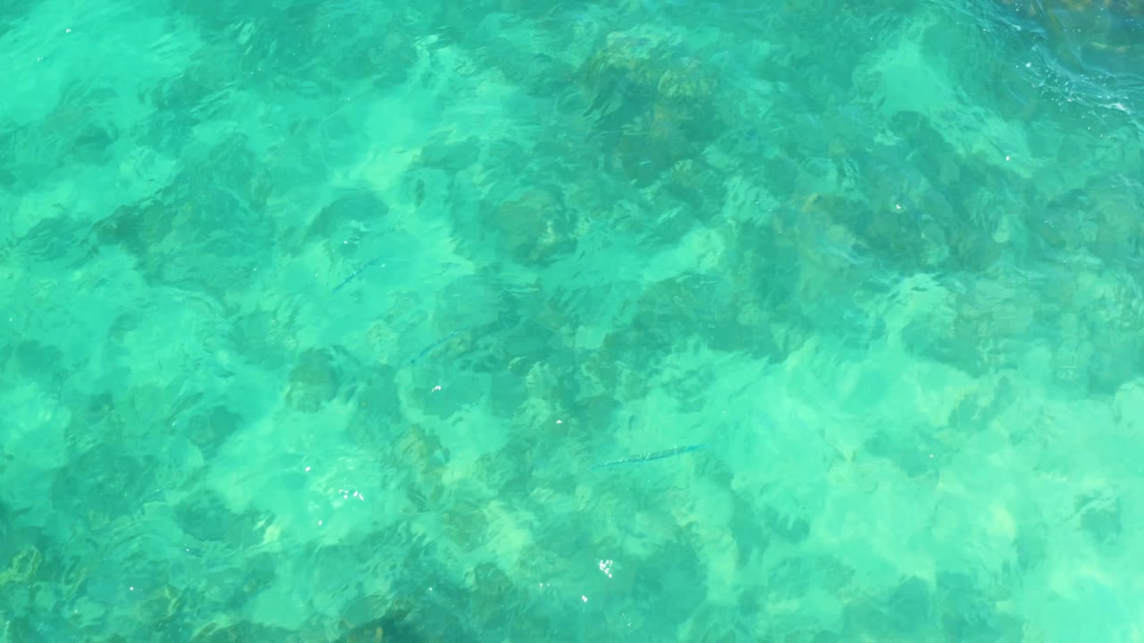 Clear water at Marquis Los Cabos, Mexico, showing darker submerged rock patches near the upper frame and lighter seabed below, with no visible people.