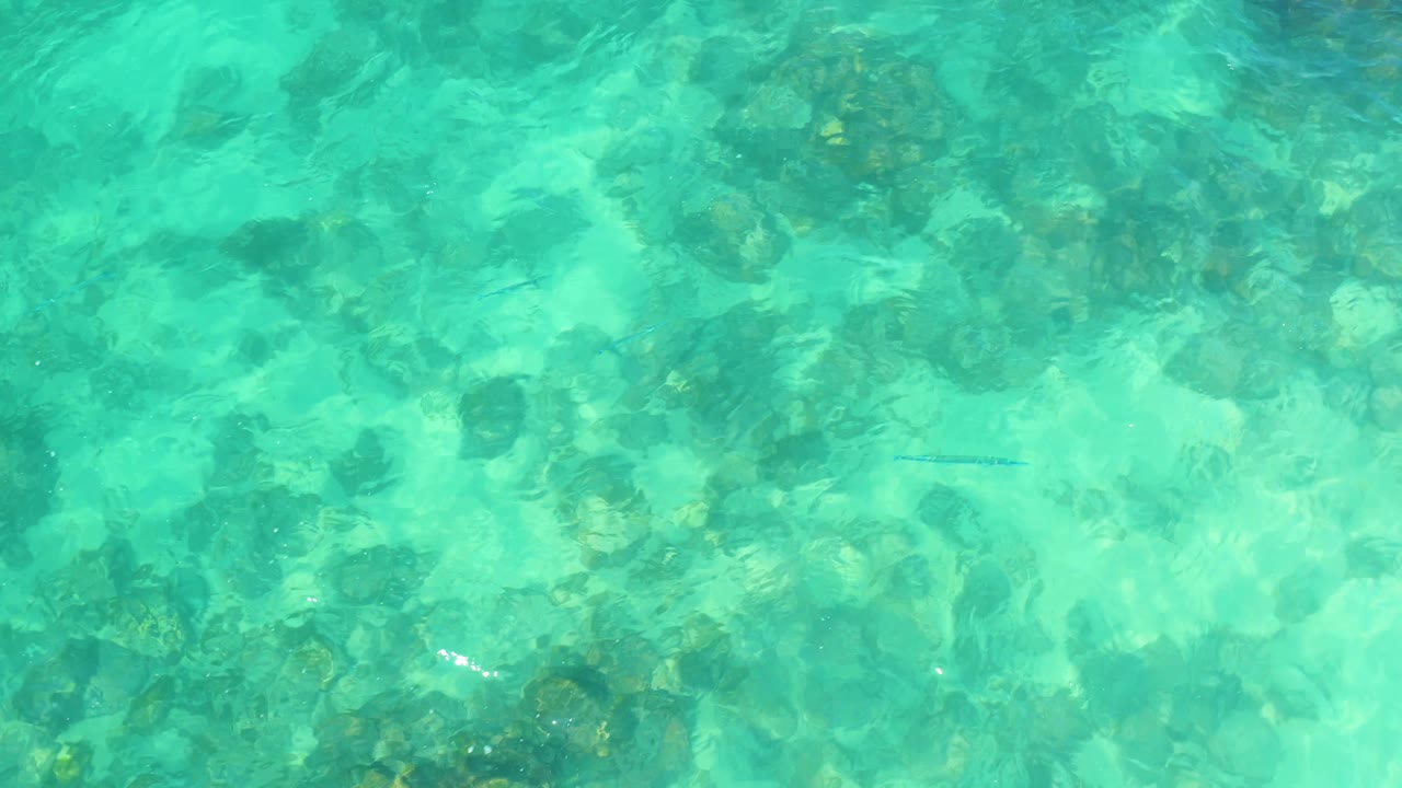 Ripples brighten the upper portion of the turquoise water while submerged rocks and sand remain visible below at Marquis Los Cabos, Mexico, with no visible people.