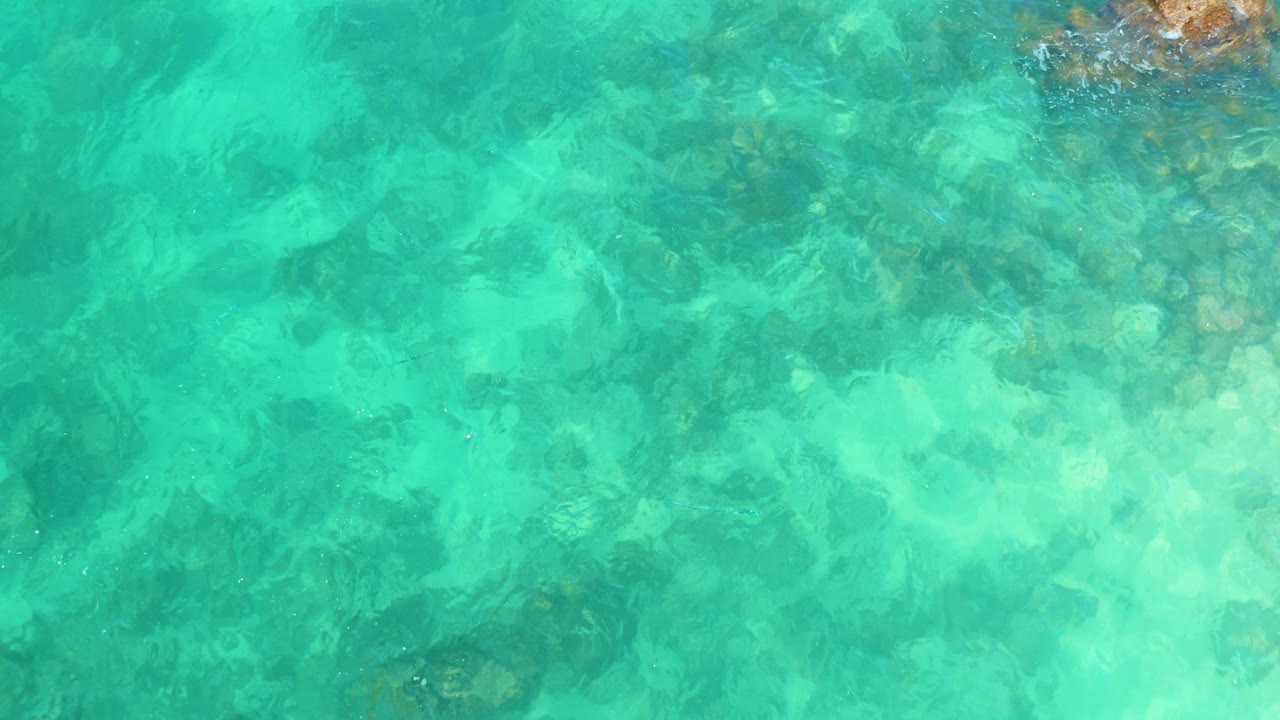 Overhead view of turquoise shallow water at Marquis Los Cabos, Mexico, with submerged rocks visible near the top of frame and no visible people.
