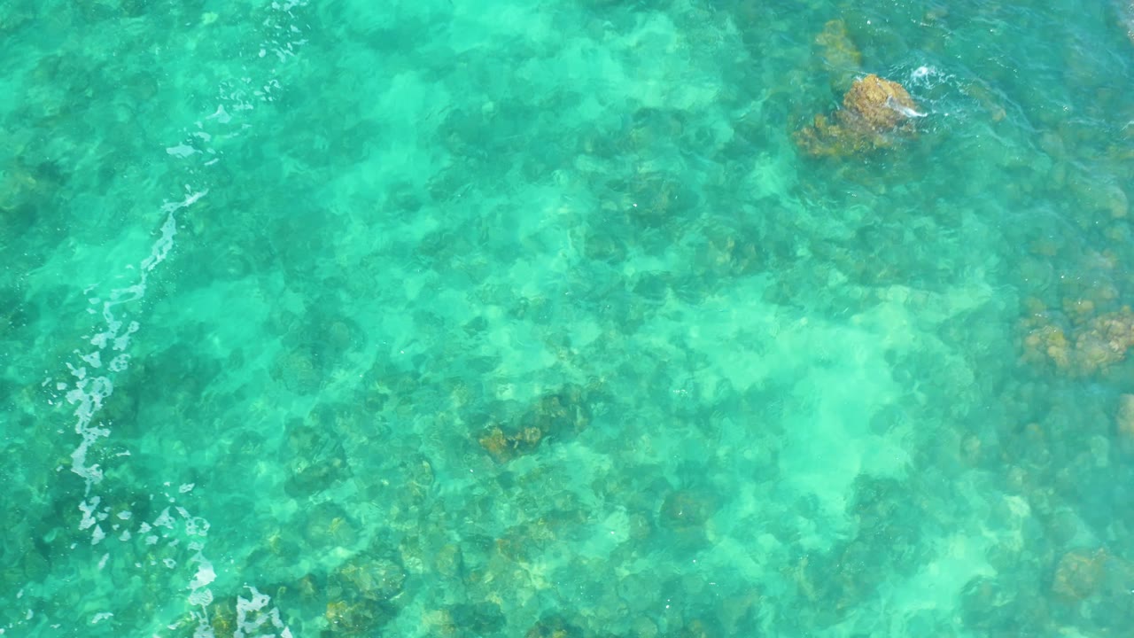 Clear green-blue water at Marquis Los Cabos, Mexico, shows a rocky seabed under a thin diagonal white ripple line, with no visible people.