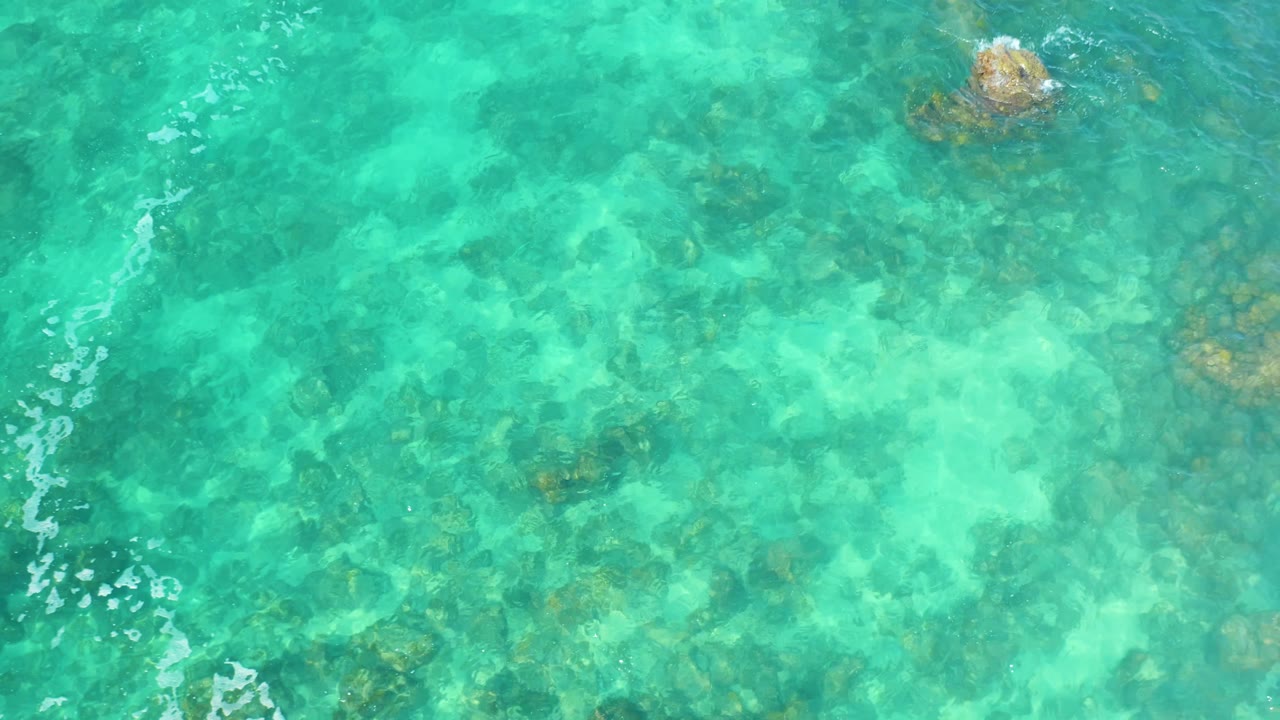 Shallow turquoise ocean water at Marquis Los Cabos, Mexico, reveals pale sandy patches and darker underwater rock clusters, with no visible people.