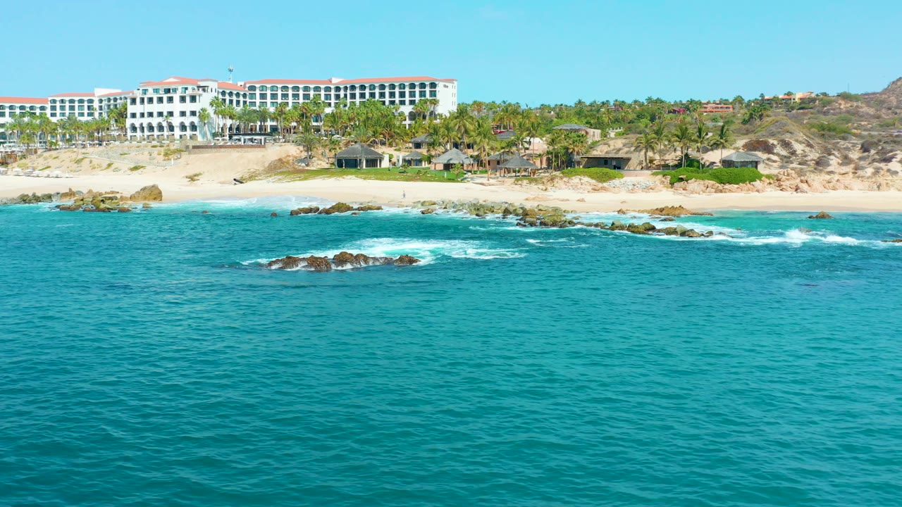 Turquoise water and shoreline rocks with resort buildings behind a palm-lined beach.