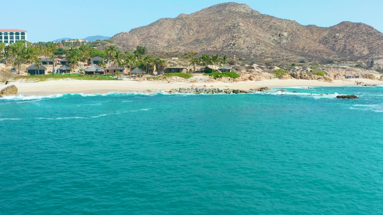 Wide beach shoreline with turquoise water and coastal buildings.
