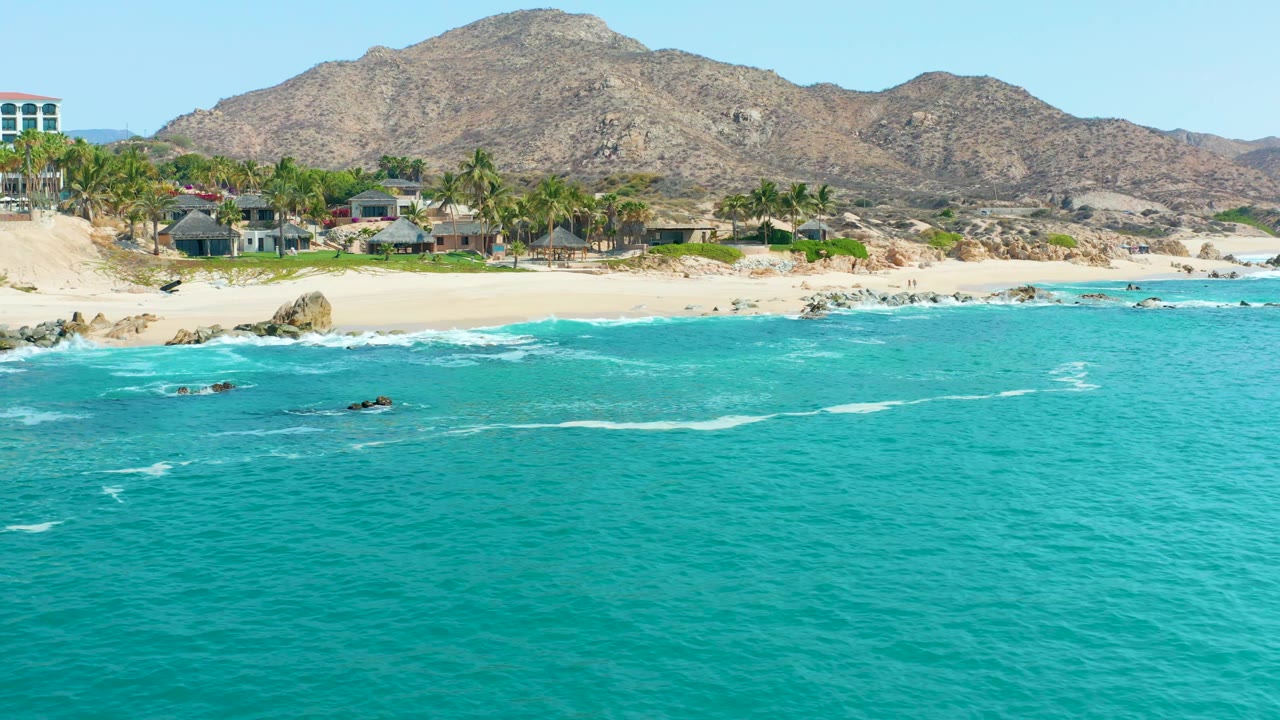 Palm-lined beach with buildings below dry mountains